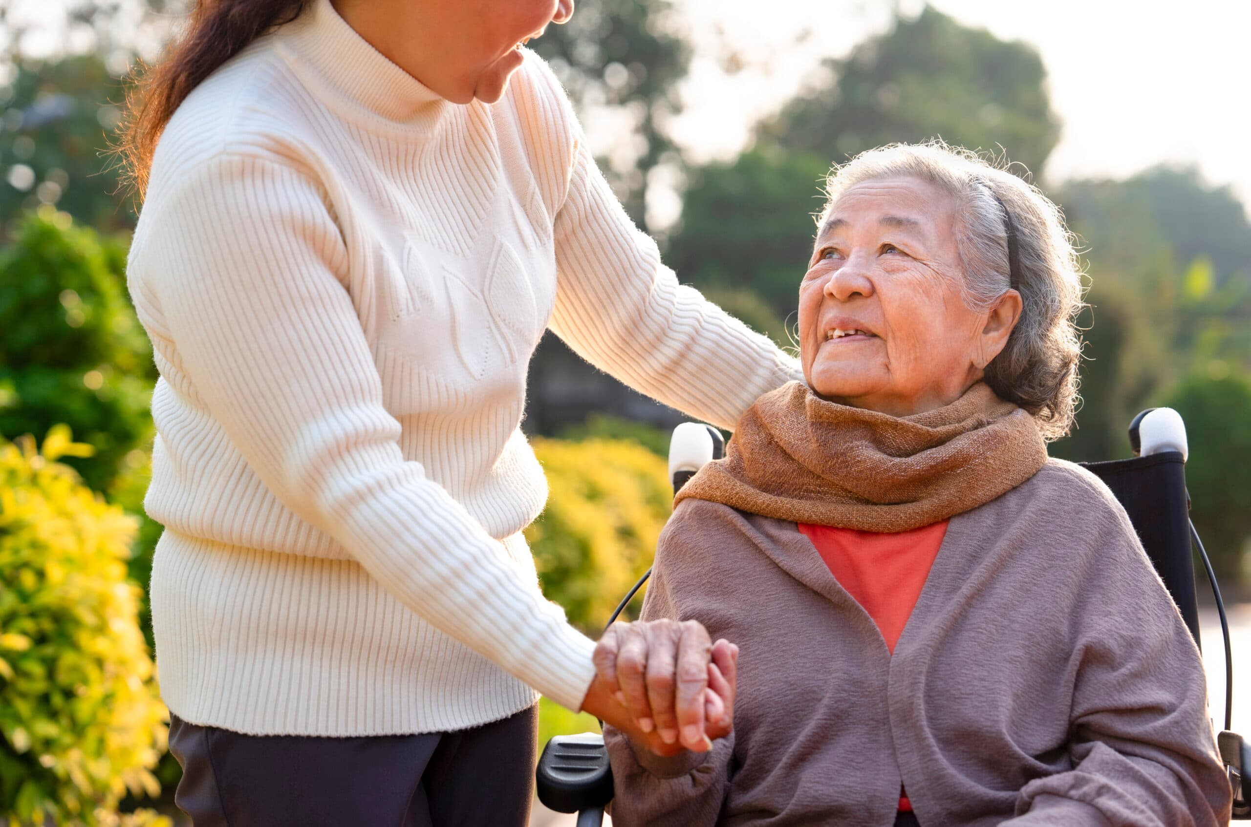 closeup happy grandma on wheelchair talking with carer in the garden in the morning sun